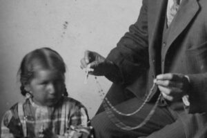 Black Elk showing a girl a Catholic rosary.